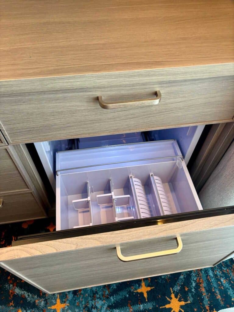 Open drawer of a dresser showcasing a mini fridge with compartments, set against a colorful carpet.