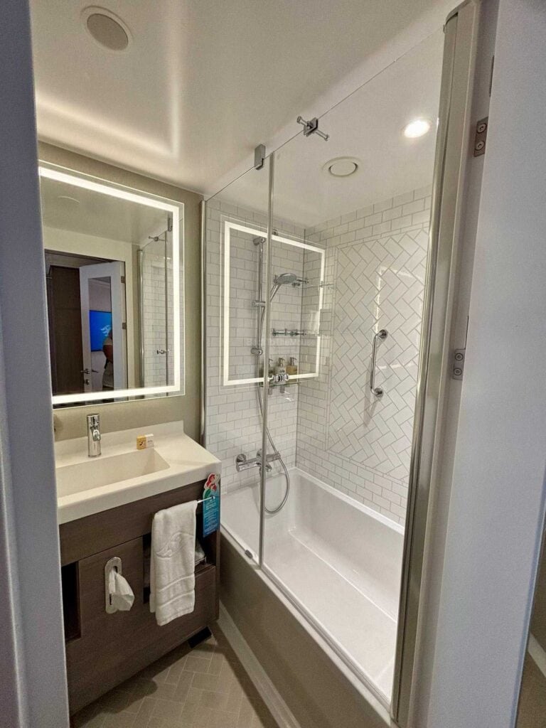 Bathroom of a Deluxe Family Oceanview Stateroom on the Disney Destiny, featuring a shower and bathtub combination, modern fixtures, and bright lighting.