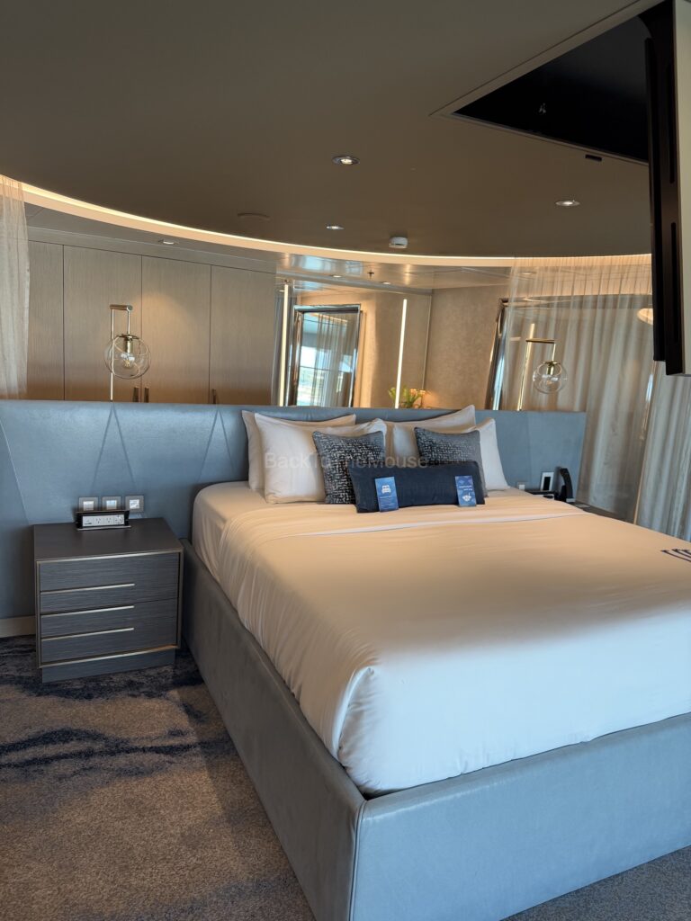 Luxurious bedroom in the Royal Loft Suite featuring a large queen-size bed with decorative pillows, a bedside table with lamps, and modern decor.