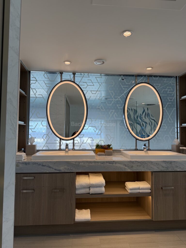 Luxurious bathroom in the Royal Loft Suite featuring double sinks, circular mirrors with backlighting, and ample storage with neatly arranged towels.