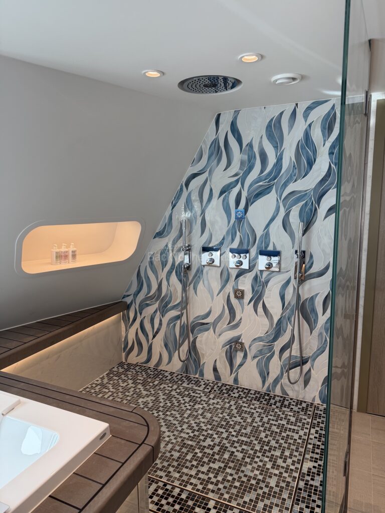 Luxurious bathroom in the Royal Loft Suite featuring a stylish shower with a wavy blue tile design, a modern sink, and wooden accents.