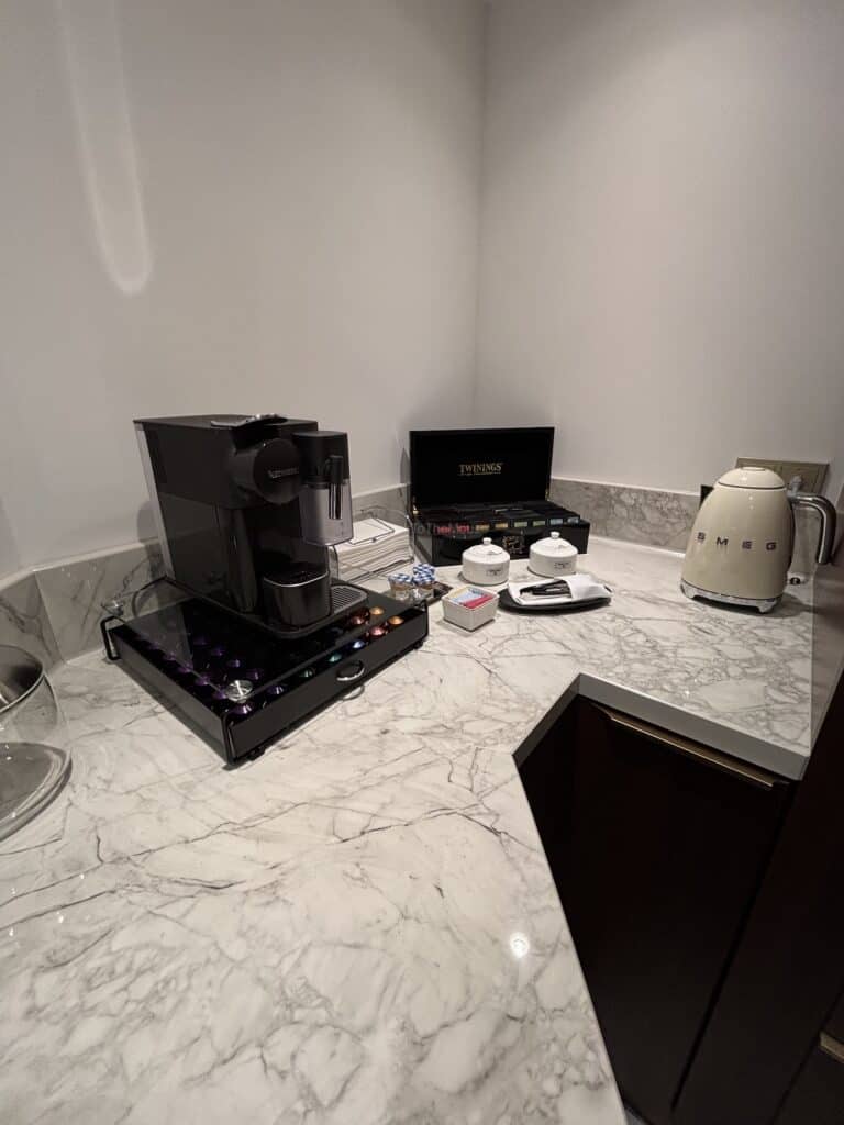 A coffee machine, kettle, and tea box setup on a marble countertop in a suite.