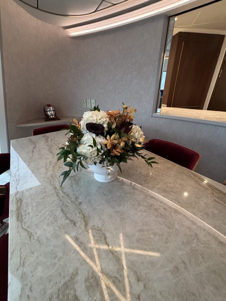 A close-up view of a luxury stateroom dining table with a bouquet of flowers in a white vase, set in an elegantly designed room.