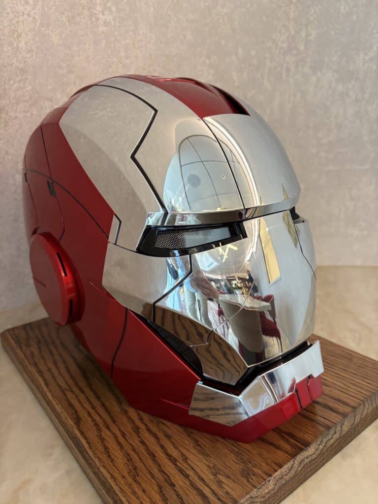 A detailed close-up of an Iron Man helmet displayed on a wooden stand, showcasing its shiny red and silver surface against a textured background.