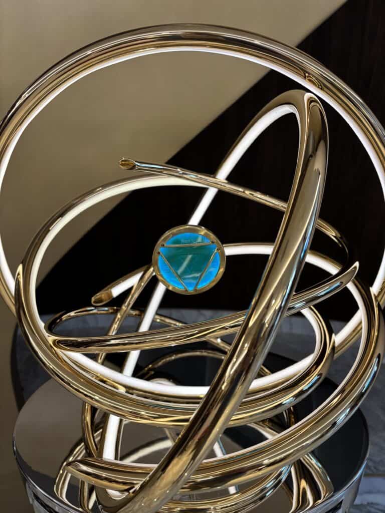 A decorative sculpture featuring intertwined metallic rings and a blue circular accent, placed on a reflective surface.