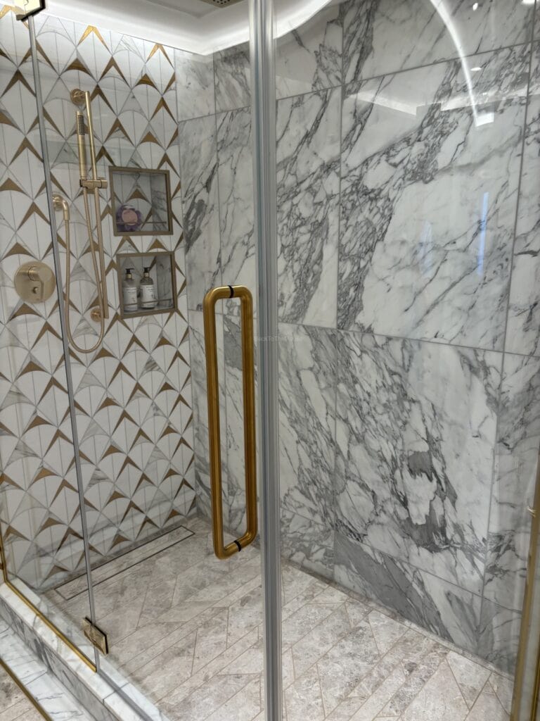 Luxurious shower area featuring marble walls and geometric patterned tiles, equipped with a gold handle and elegant fixtures.
