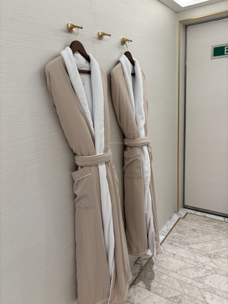 Two beige bathrobes hanging on hooks against a light-colored wall in a luxurious setting.