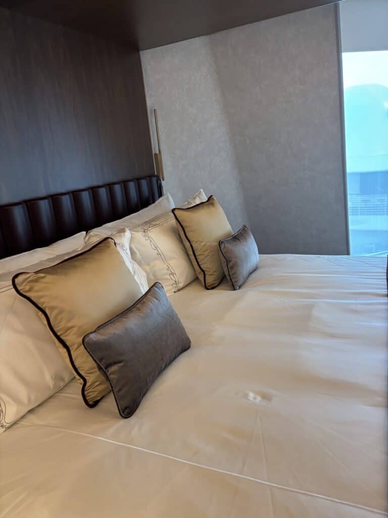 Interior of a luxurious stateroom featuring a large bed with decorative pillows and a contemporary design.