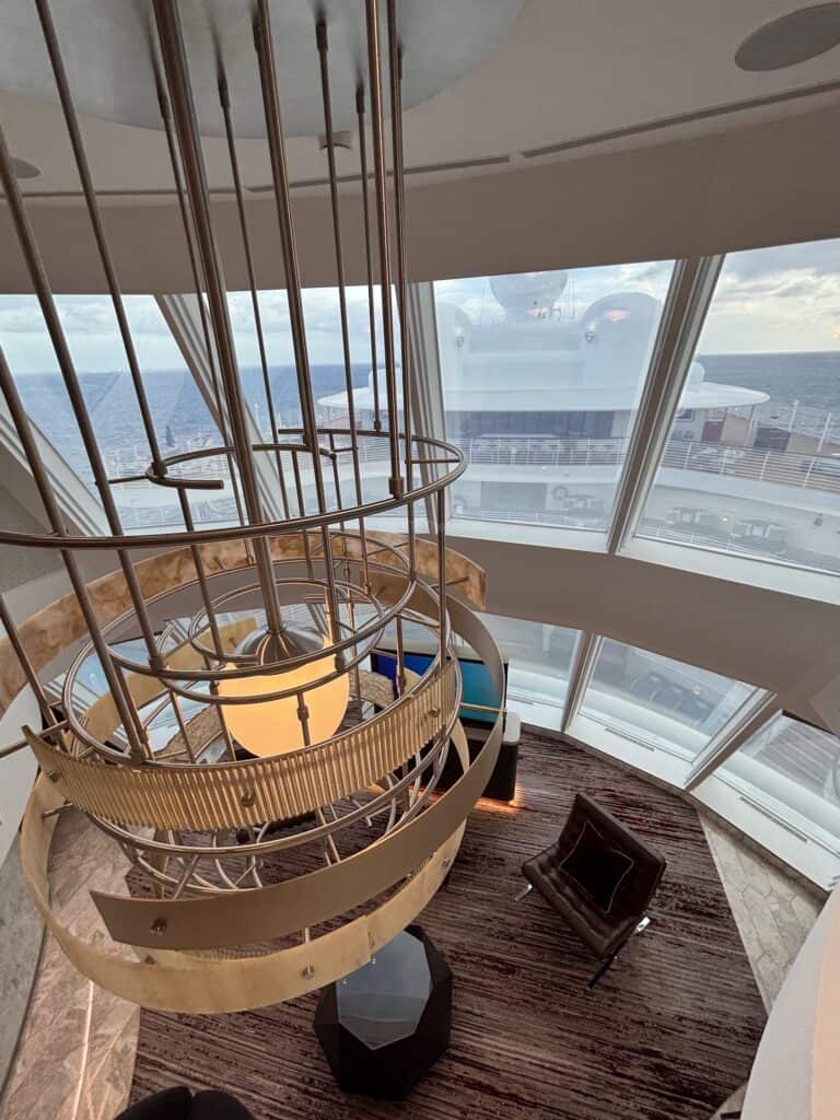 View from above of the Concierge Tower Suite on the Disney Destiny, showcasing a modern chandelier, a cozy seating area, and large windows with an ocean view.