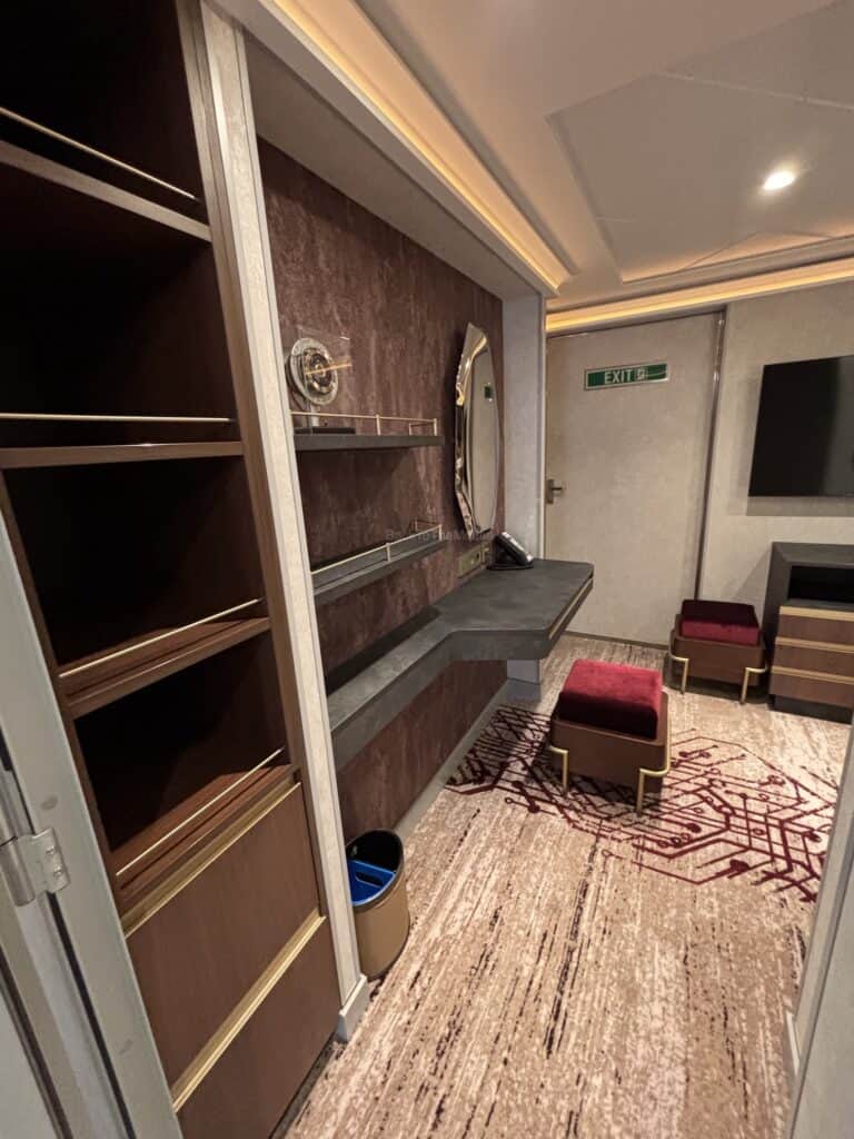 Interior view of Stateroom 14000 on the Disney Destiny, showcasing an open space with a wall mirror, shelves, and seating area.