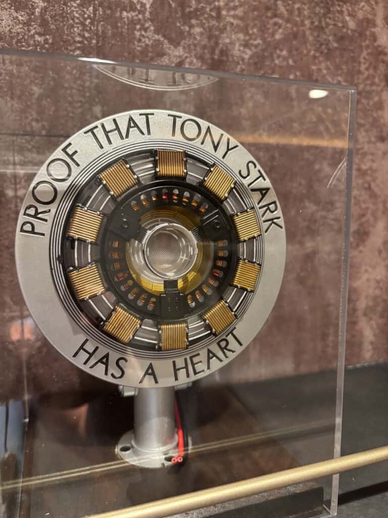 A display featuring a circular device with the inscription 'PROOF THAT TONY STARK HAS A HEART'. The device is intricately designed with metallic details and a translucent center, contained within a clear case.