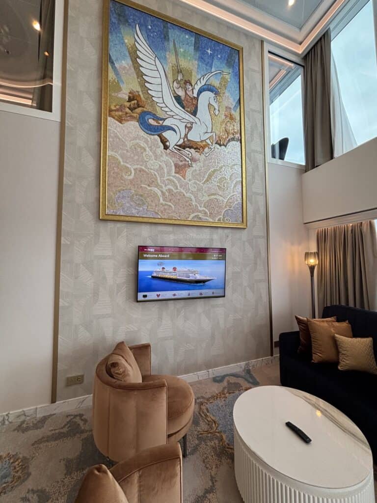 Interior view of a luxurious stateroom featuring a large mural of a winged horse on the wall, a TV mounted on the wall, plush seating, and elegant decor.