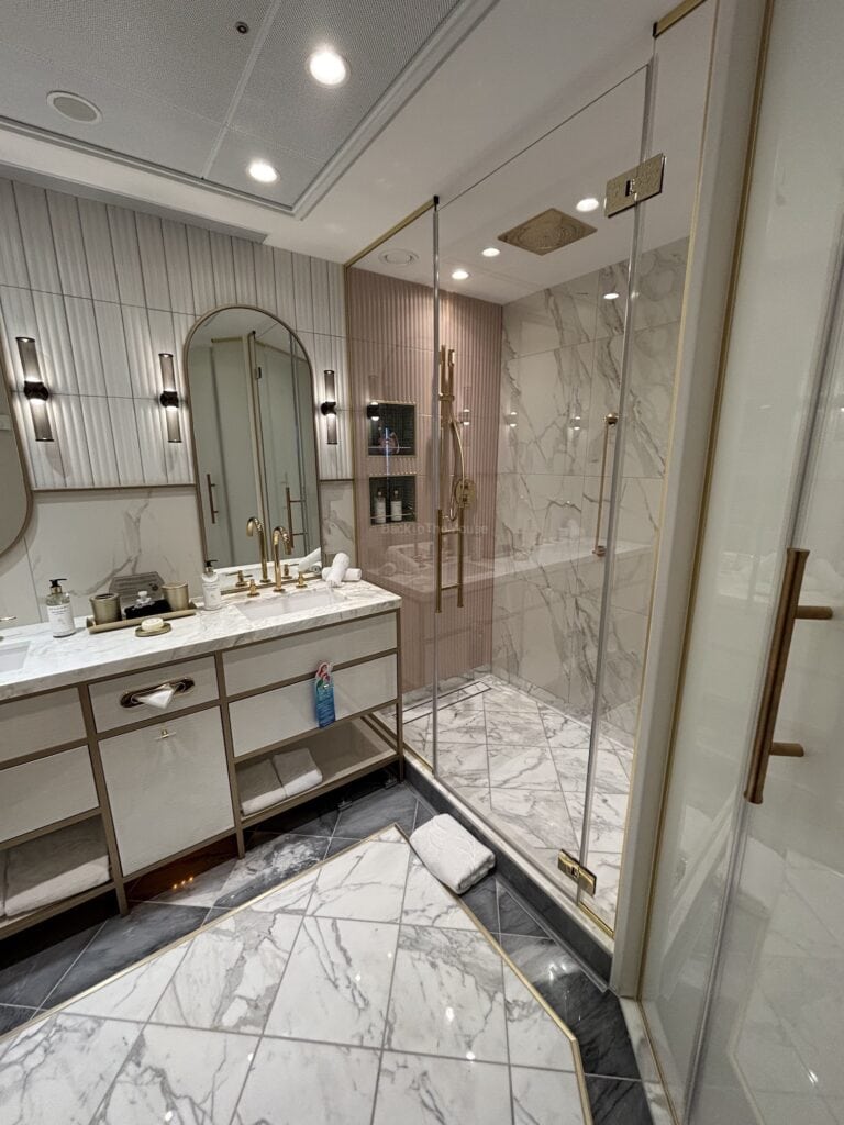 Luxurious bathroom with marble flooring, double vanity sinks, gold fixtures, and a glass shower enclosure.