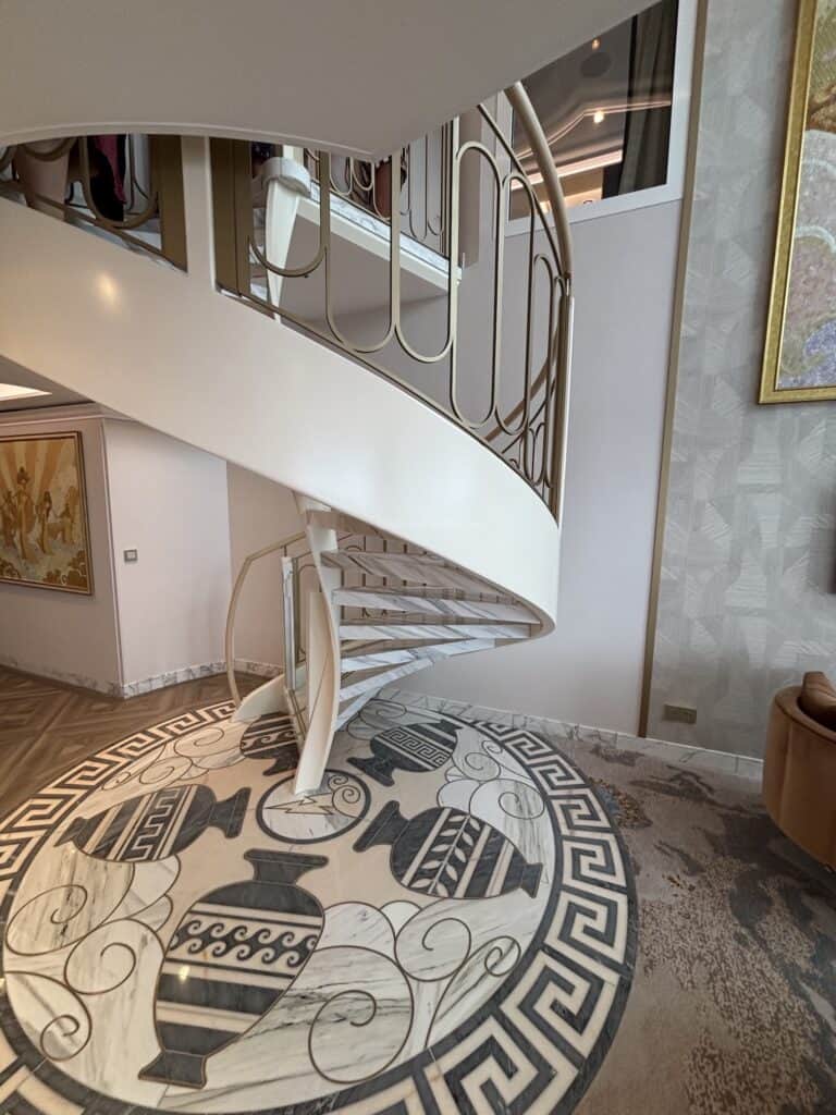 A spiral staircase with a decorative floor featuring a circular design of vases and intricate patterns, shown from the base looking up.