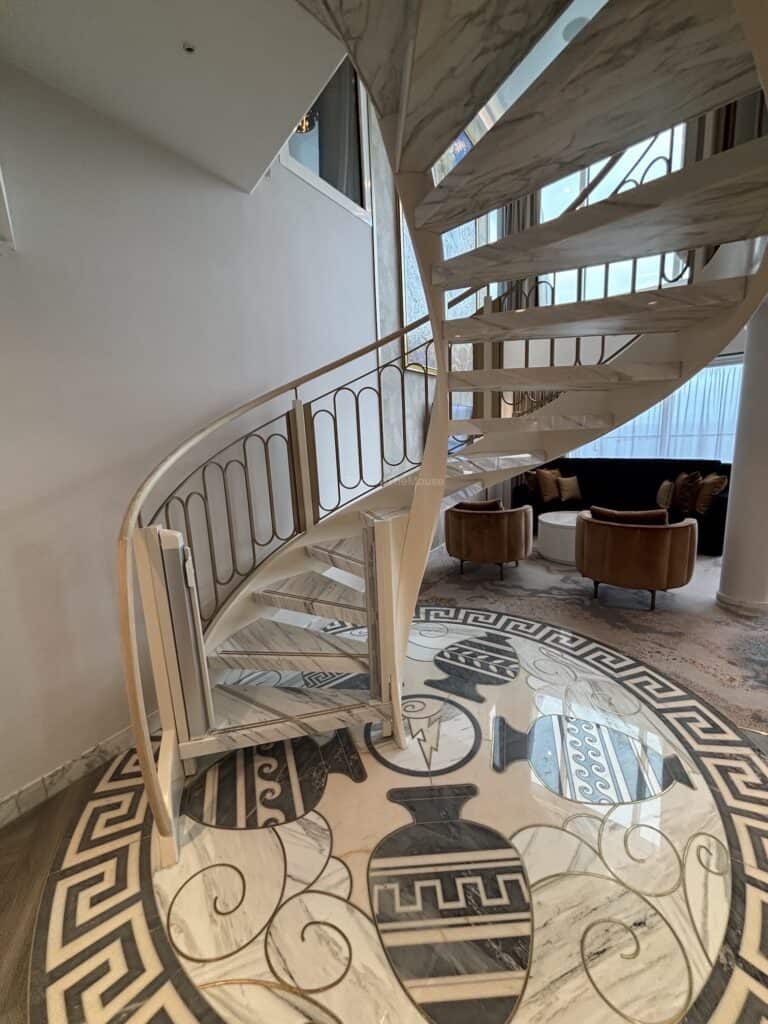 A spiral staircase leading to the upper level of a luxurious suite, surrounded by elegant decor and marble flooring featuring intricate designs.