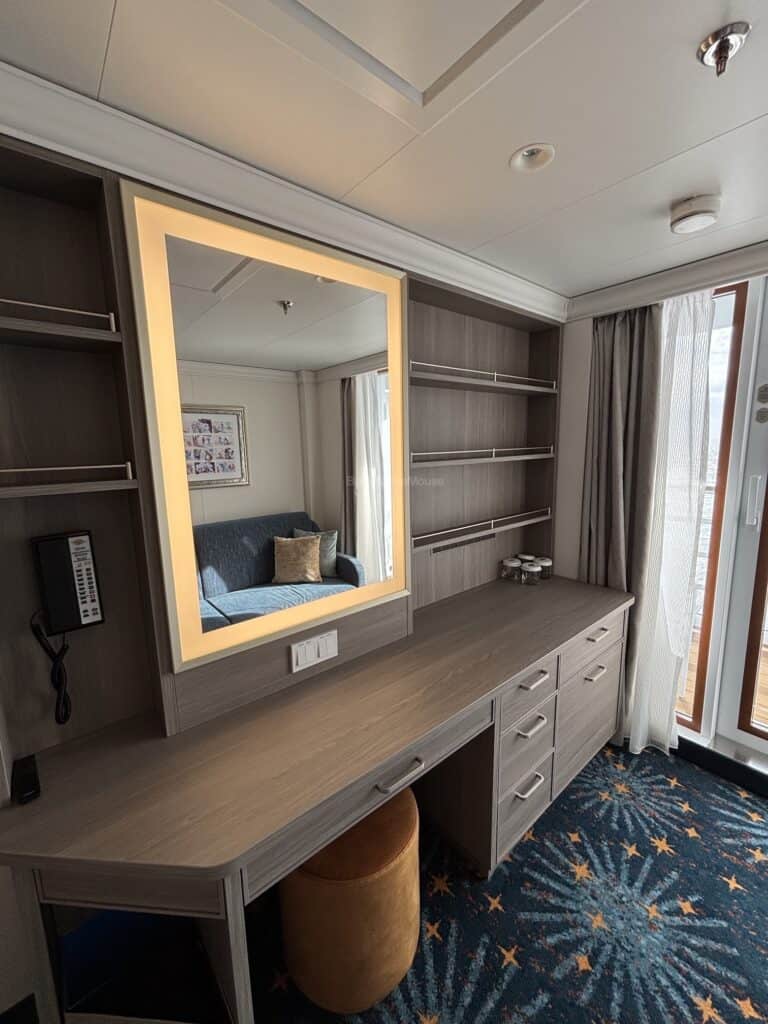 Interior view of a Deluxe Oceanview Stateroom with a vanity area, a blue couch, and a balcony door.