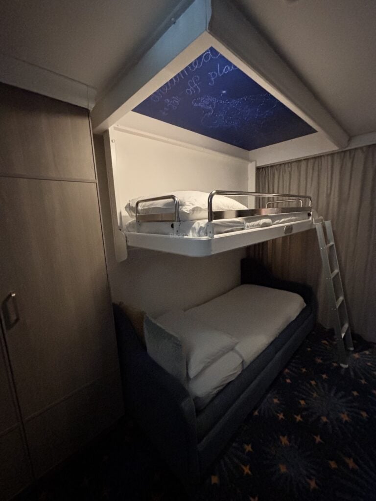 Interior view of a Deluxe Family Oceanview Stateroom on the Disney Destiny, featuring a pull-down bed and a couch bed.