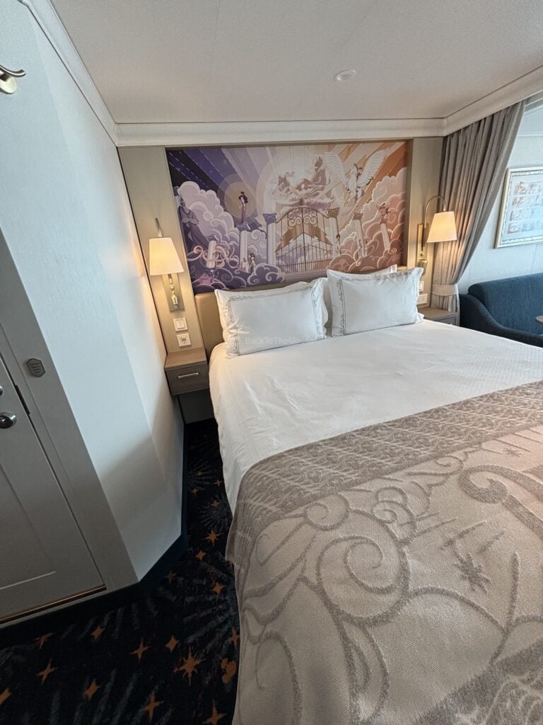 Interior view of a Deluxe Family Oceanview Stateroom on the Disney Destiny, featuring a bed with decorative pillows and a wall mural.