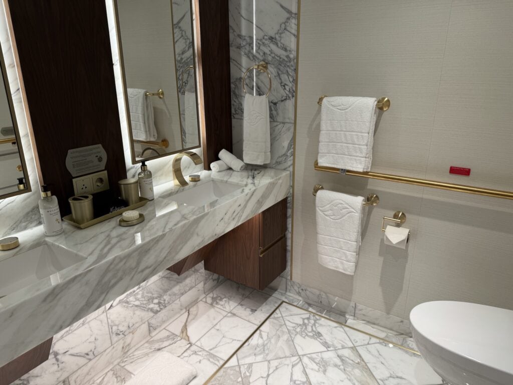 A luxurious bathroom featuring a double marble sink, stylish gold fixtures, mirrored cabinets, and neatly arranged towels, with modern amenities.