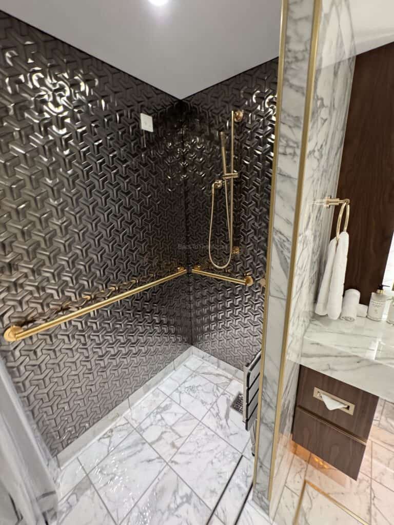 Interior view of a luxurious shower with gold fixtures and textured black tiles, showcasing marble flooring and a stylish design.