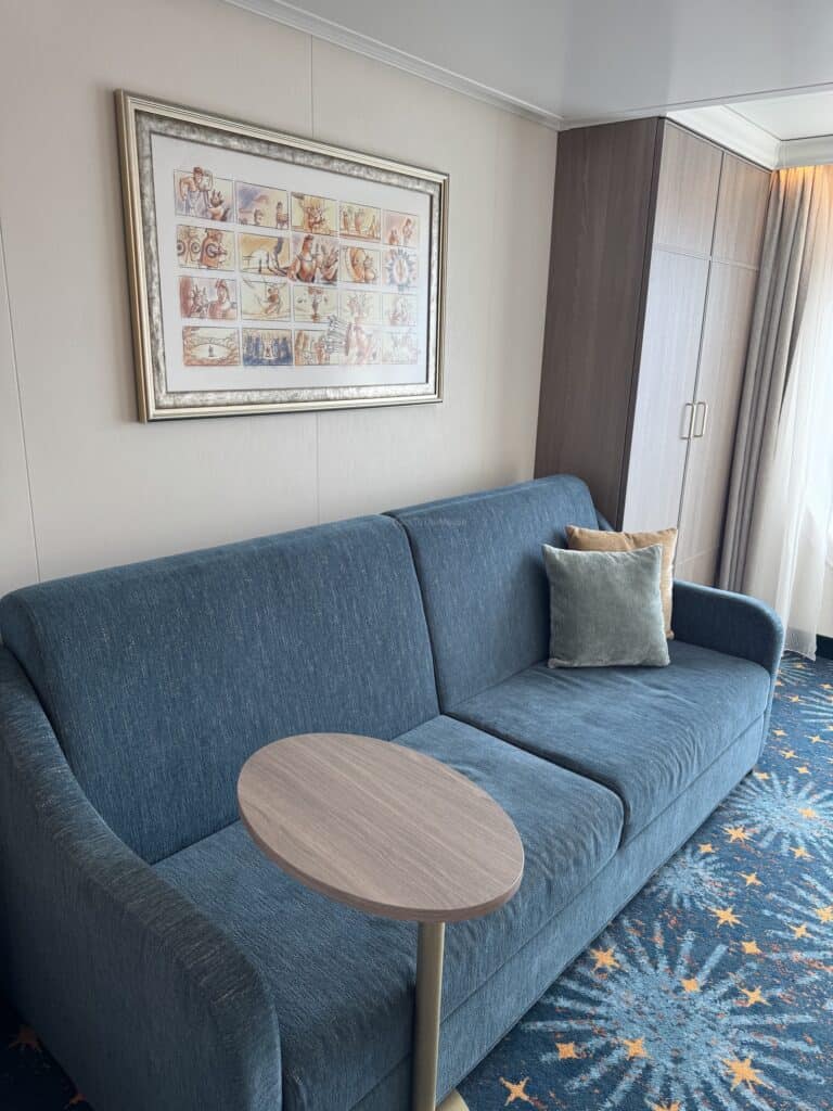 A cozy blue sofa with a decorative pillow, accompanied by a small oval table, set against soft beige walls and a piece of framed artwork above the sofa.