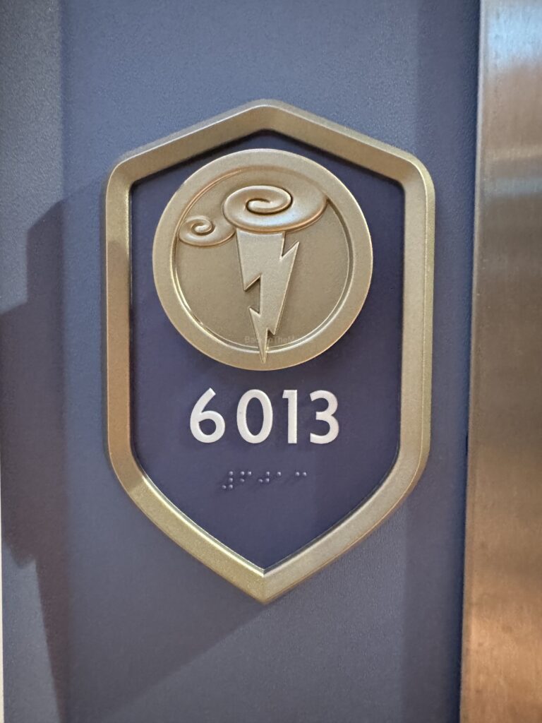 Close-up of the door sign for stateroom 6013 on the Disney Destiny, featuring a stylized emblem and the room number.