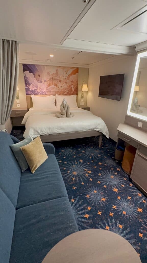 Interior view of a 11B Standard Inside Stateroom on the Disney Destiny featuring a bed, decorative mural, seating area, and television.