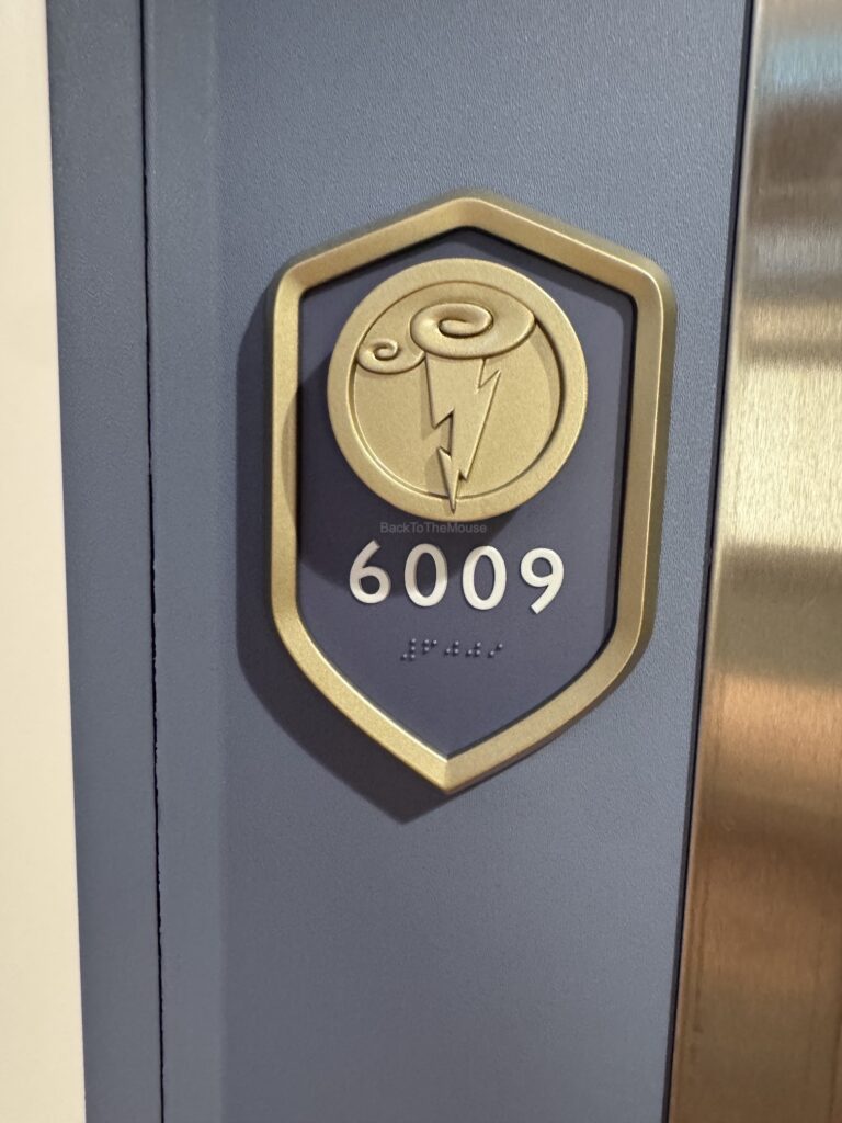Close-up of the door number plaque for Stateroom 6009 on the Disney Destiny, featuring a design with a swirling cloud and lightning symbol.