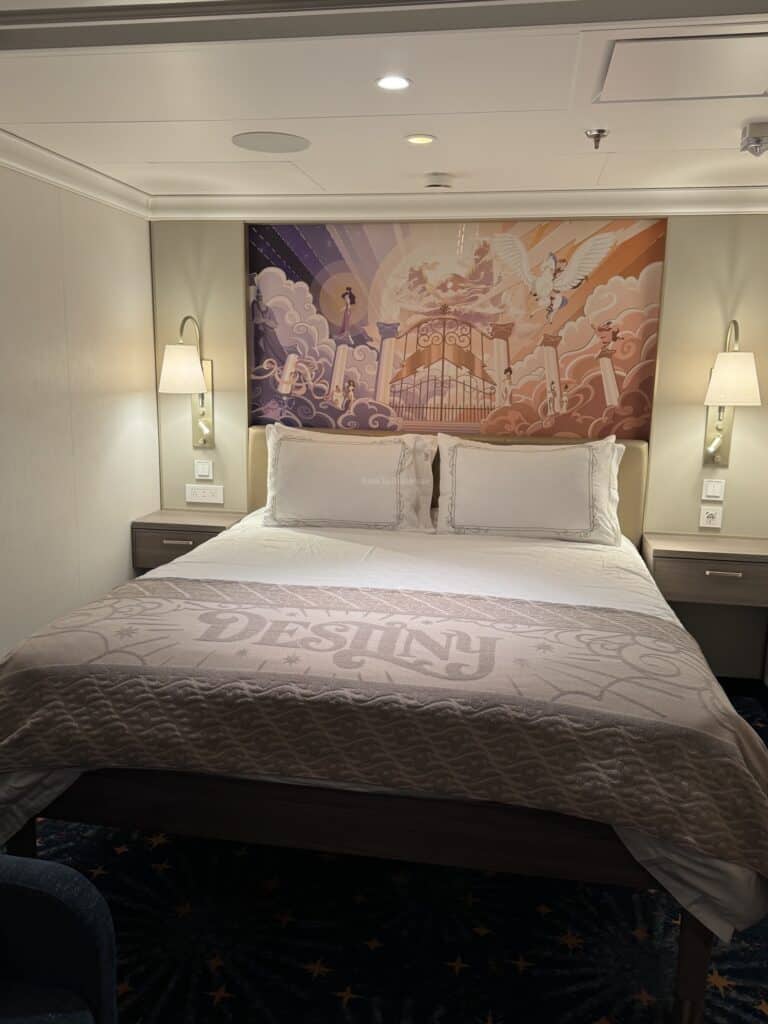 Interior view of Stateroom 6009 on the Disney Destiny, featuring a large bed with a 'DESTINY' blanket and decorative wall art.
